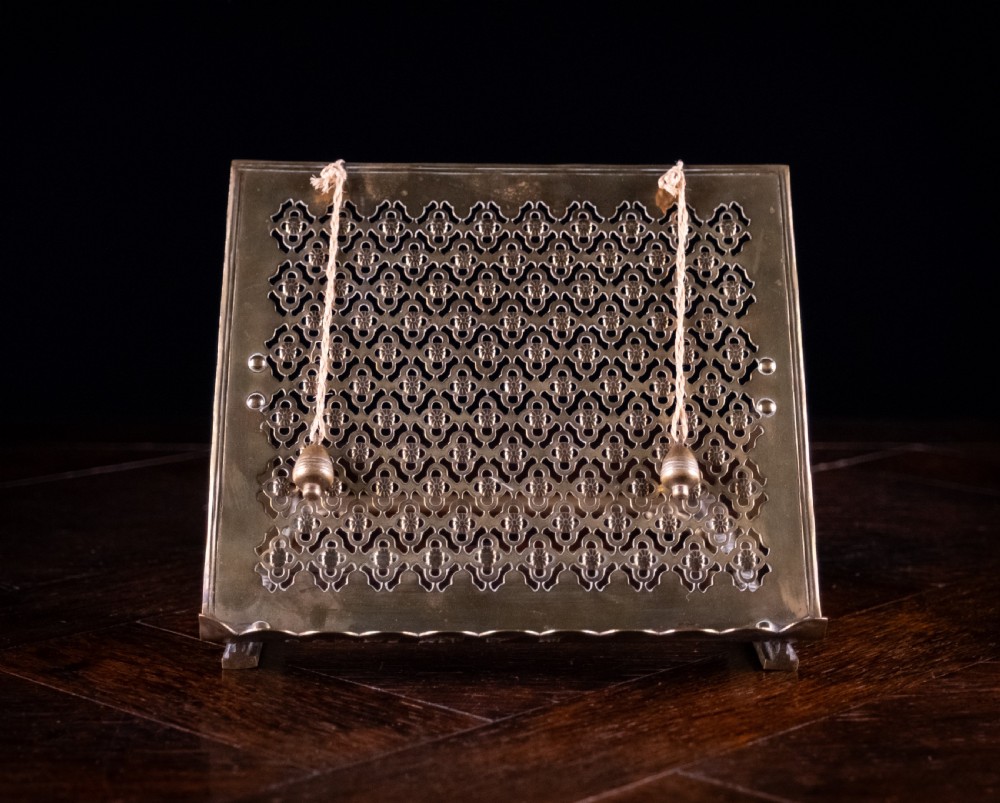An antique brass folding book rest featuring an intricate pierced fretwork pattern, adjustable easel backing, and weighted page holder cords. View VI