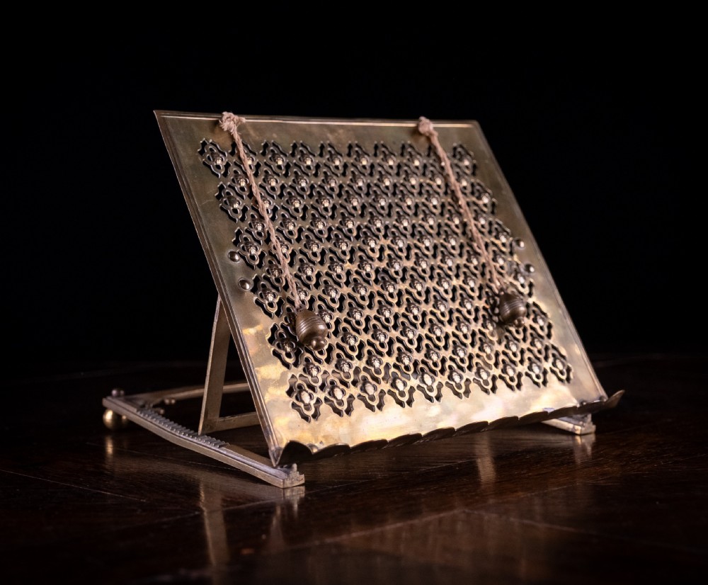 An antique brass folding book rest featuring an intricate pierced fretwork pattern, adjustable easel backing, and weighted page holder cords. View VII