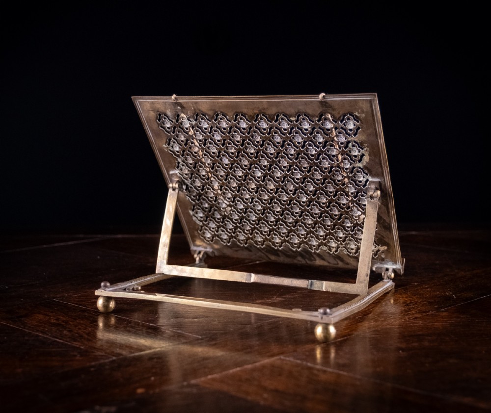 An antique brass folding book rest featuring an intricate pierced fretwork pattern, adjustable easel backing, and weighted page holder cords. View IX