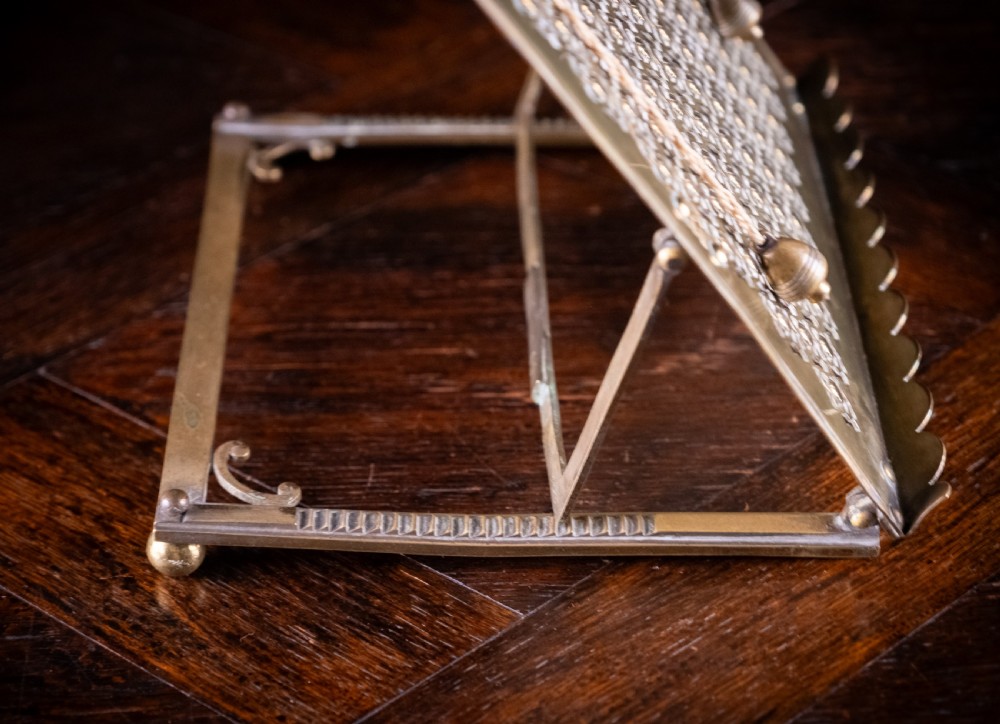 An antique brass folding book rest featuring an intricate pierced fretwork pattern, adjustable easel backing, and weighted page holder cords. View XII
