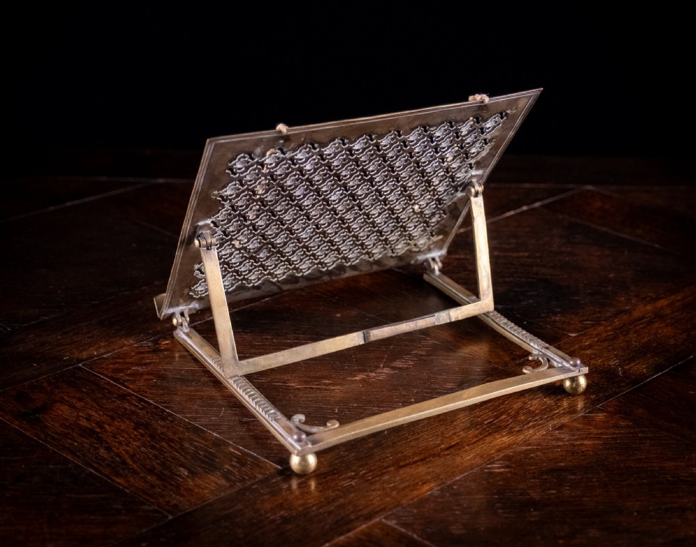 An antique brass folding book rest featuring an intricate pierced fretwork pattern, adjustable easel backing, and weighted page holder cords. View XIII