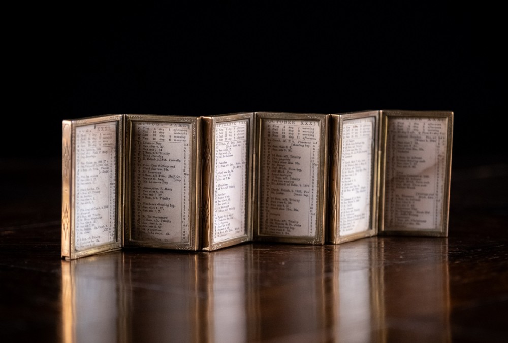 A nineteenth-century six-fold miniature brass frame holding printed paper London almanac sheets dated 1878.