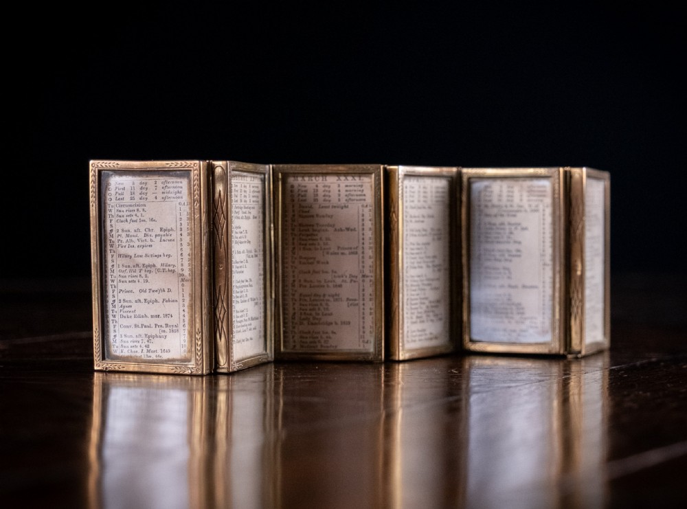 A nineteenth-century six-fold miniature brass frame holding printed paper London almanac sheets dated 1878. View IV
