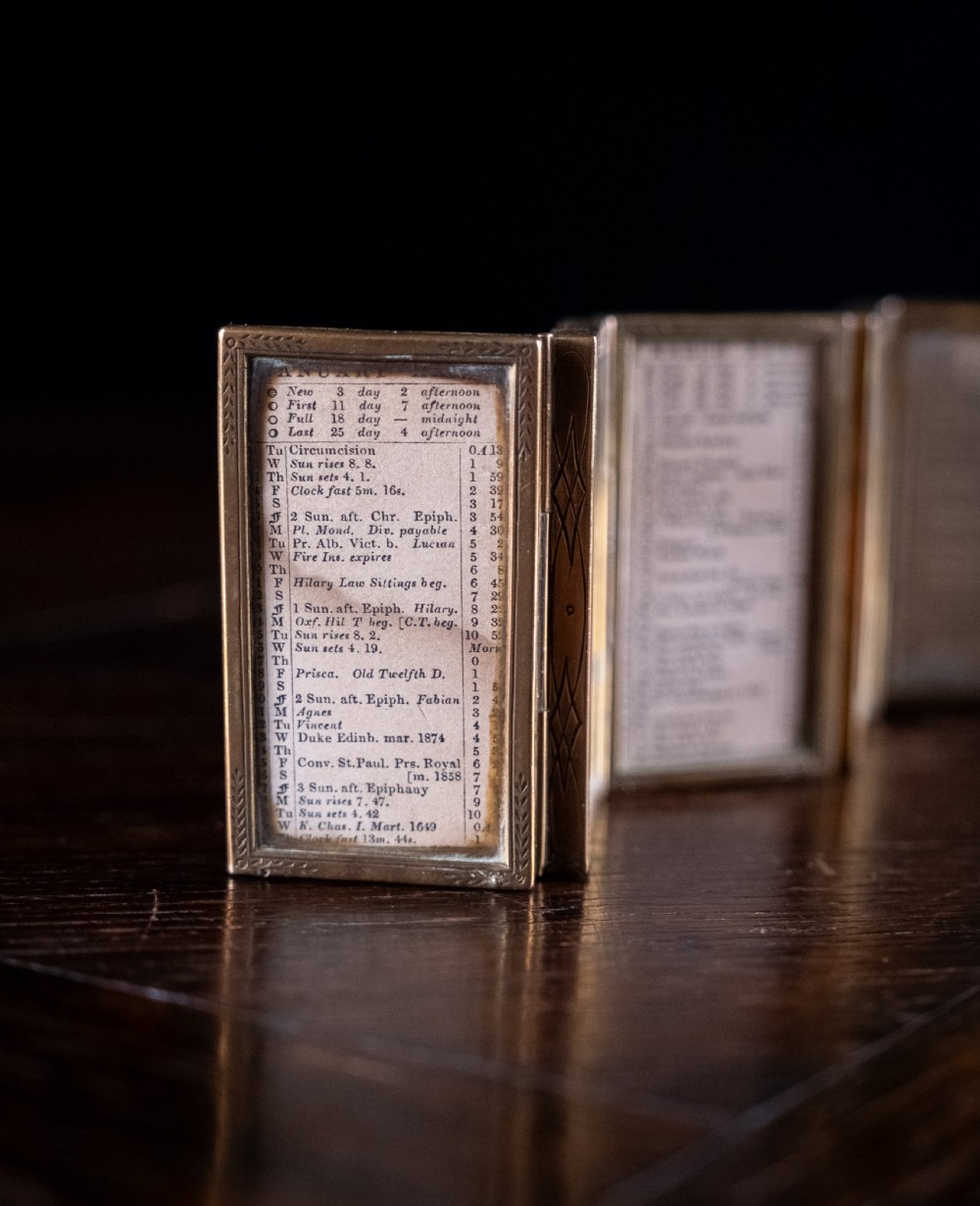 A nineteenth-century six-fold miniature brass frame holding printed paper London almanac sheets dated 1878. View IX