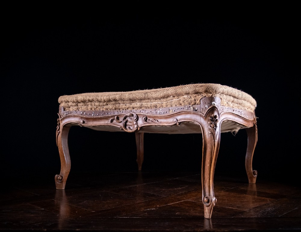 A low rectangular Louis XV style footstool featuring a carved beech frame, cabriole legs, shell motifs, and hessian upholstery.