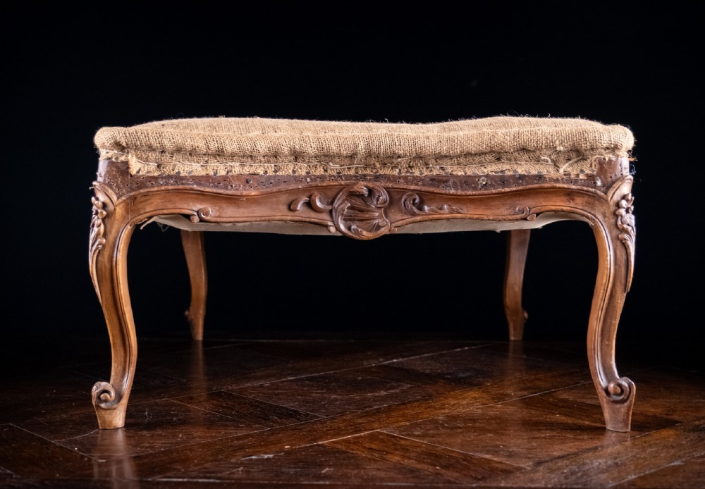A low rectangular Louis XV style footstool featuring a carved beech frame, cabriole legs, shell motifs, and hessian upholstery. View VII