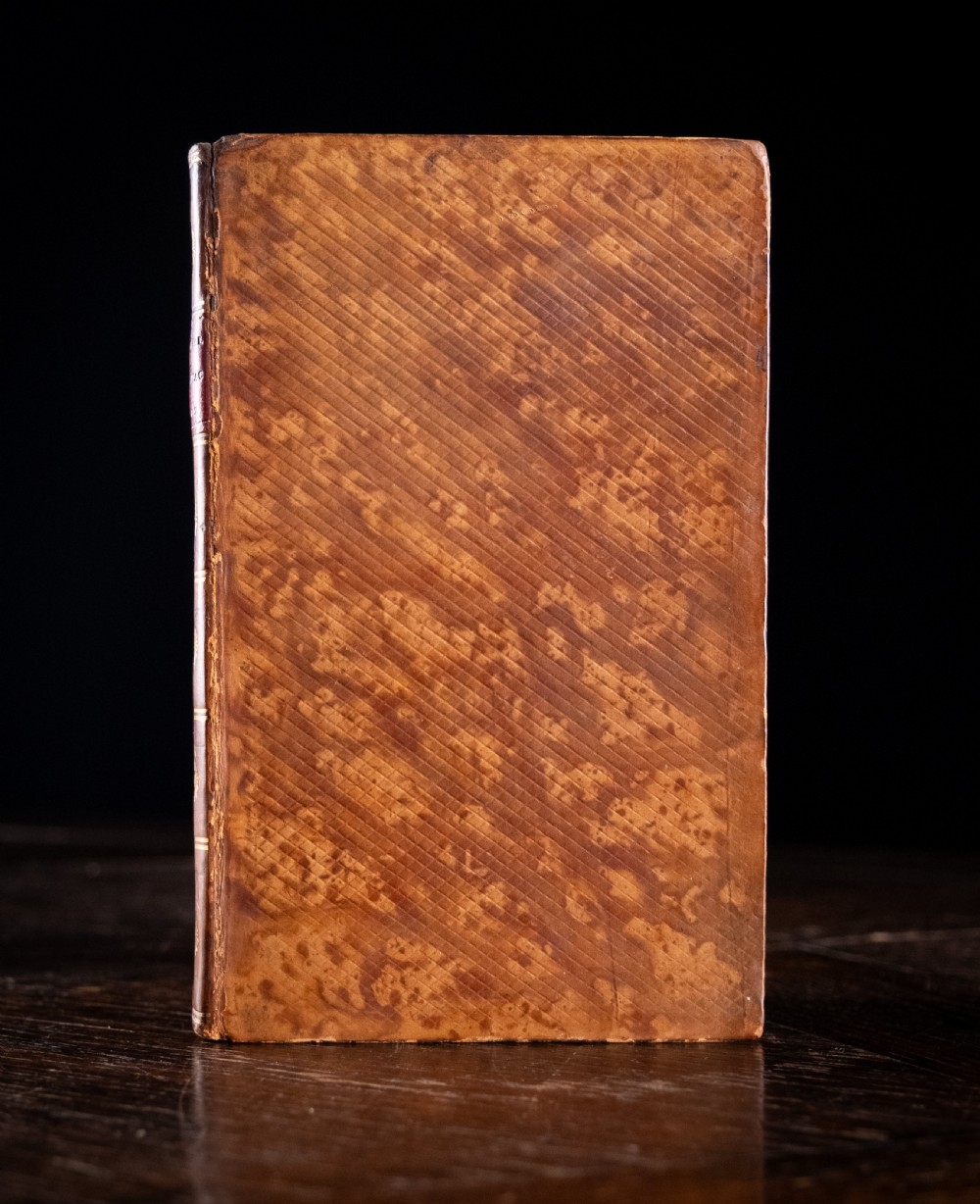 A leather-bound Georgian book standing upright, featuring a tan marbled finish, a red leather spine label with gold lettering, and gilt solar star motifs along the spine. View II