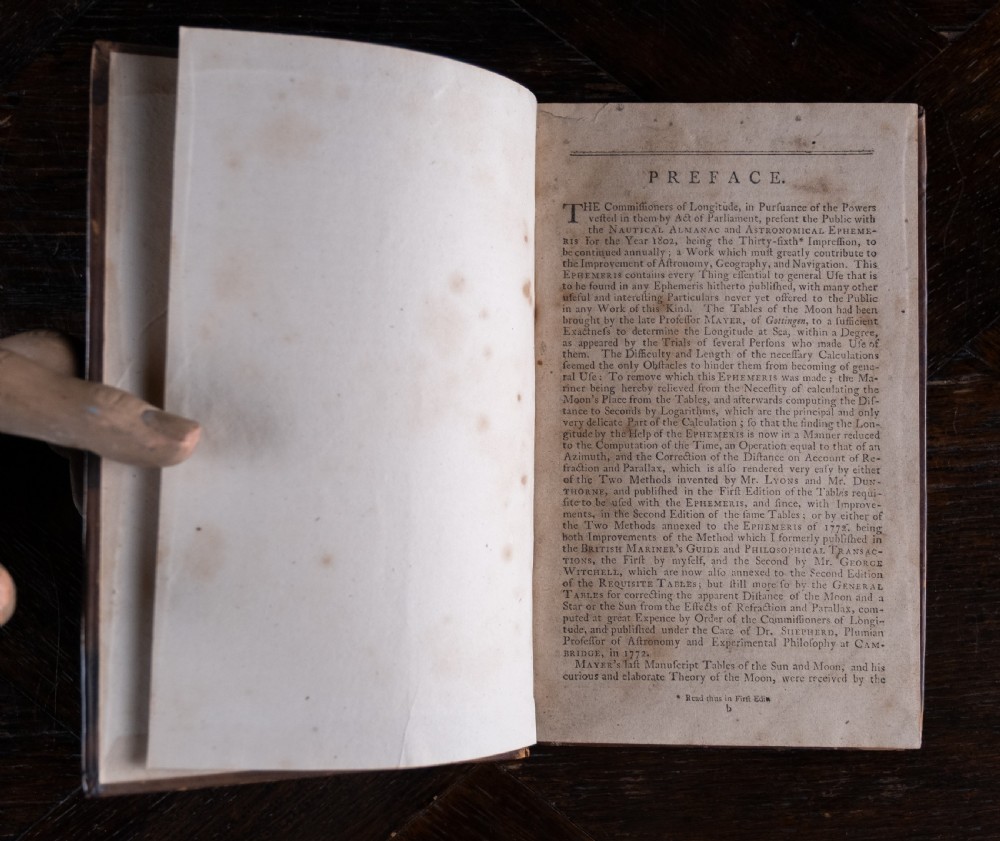 A leather-bound Georgian book standing upright, featuring a tan marbled finish, a red leather spine label with gold lettering, and gilt solar star motifs along the spine. View V