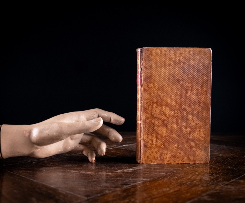 A leather-bound Georgian book standing upright, featuring a tan marbled finish, a red leather spine label with gold lettering, and gilt solar star motifs along the spine. View XI
