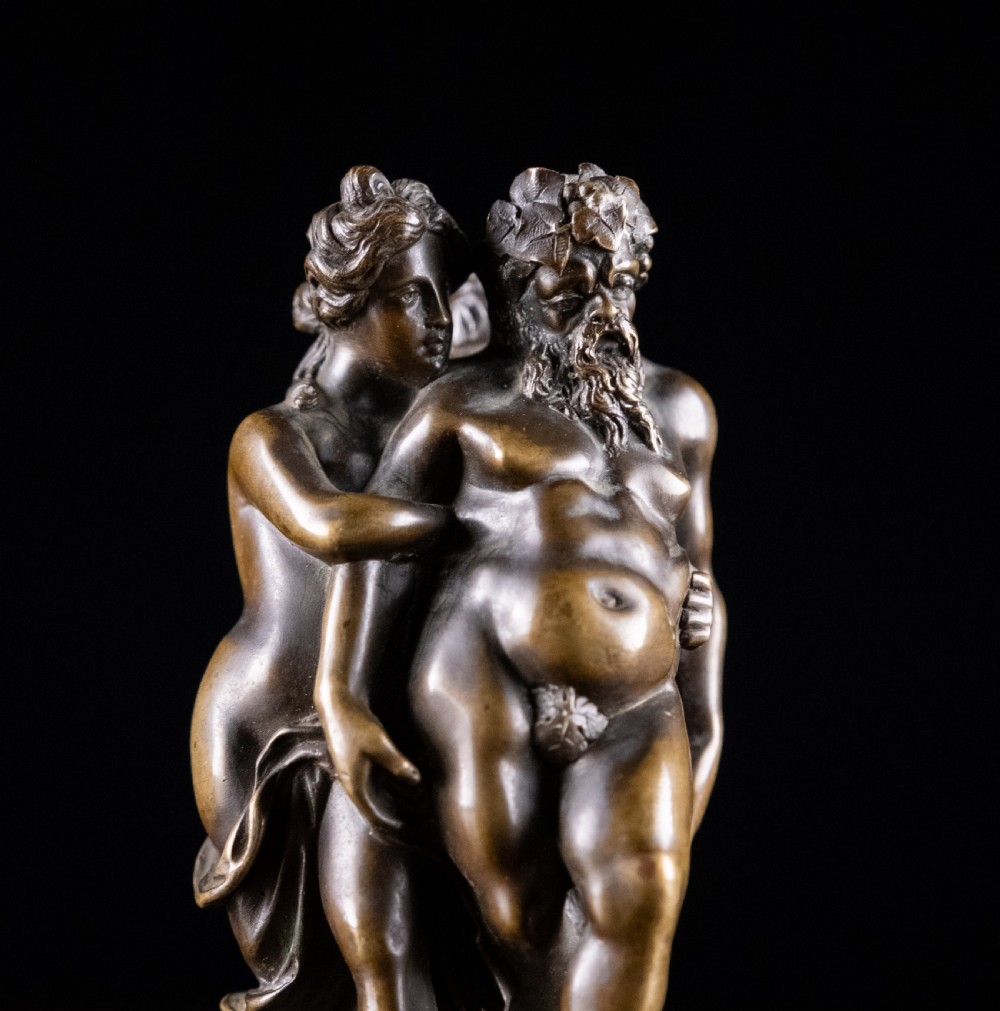 A dark brown bronze figurative sculpture group depicting Silenus supported by Pan and a Nereid on a textured bronze base. View III