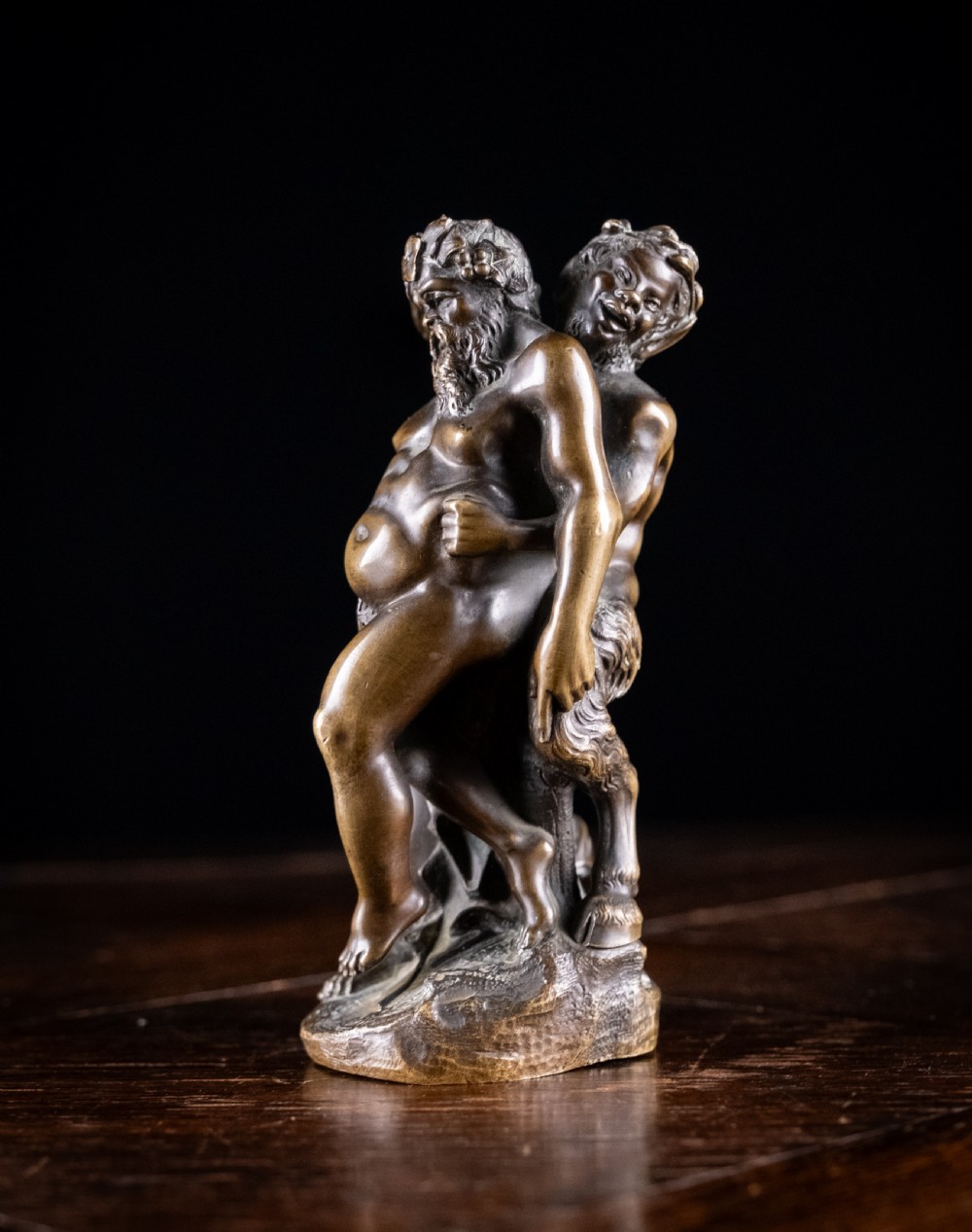 A dark brown bronze figurative sculpture group depicting Silenus supported by Pan and a Nereid on a textured bronze base. View VI