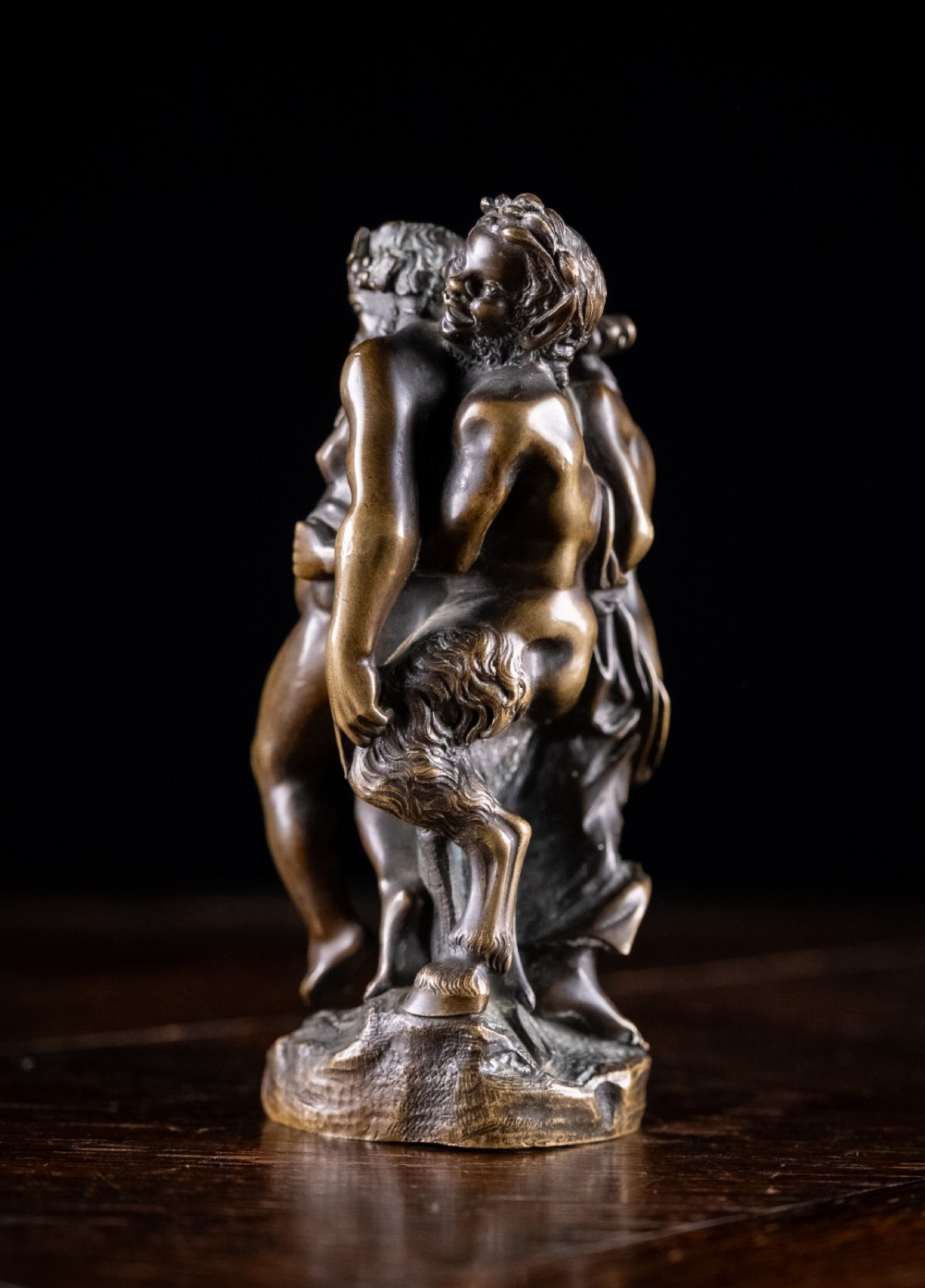 A dark brown bronze figurative sculpture group depicting Silenus supported by Pan and a Nereid on a textured bronze base. View VII