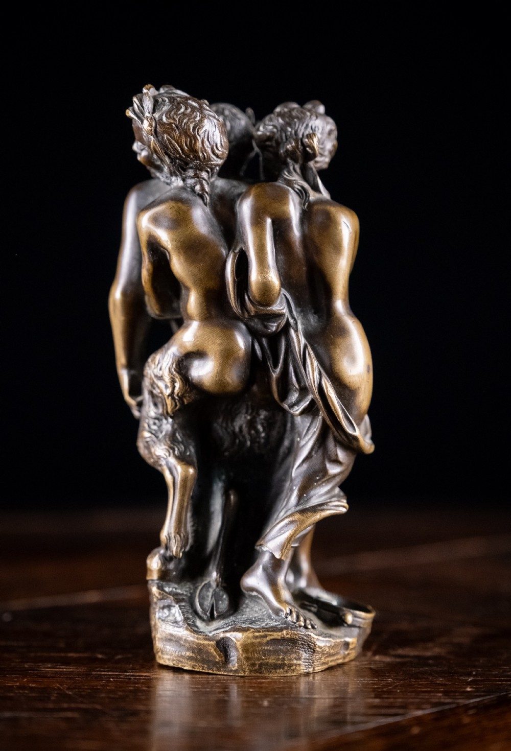 A dark brown bronze figurative sculpture group depicting Silenus supported by Pan and a Nereid on a textured bronze base. View VIII