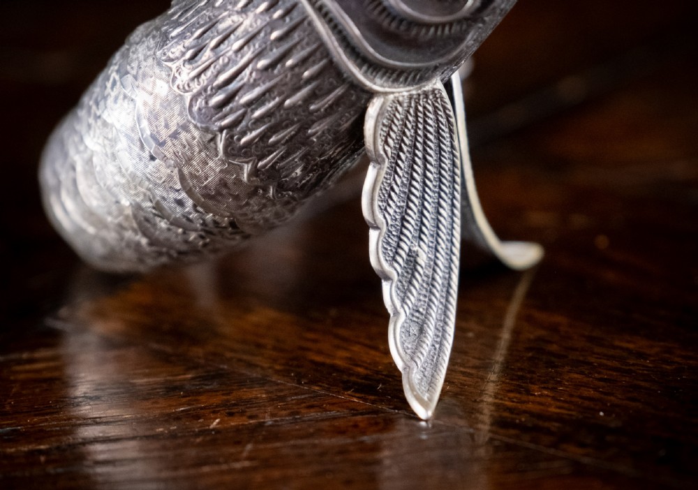 An articulated silver swordfish figure with detailed scales, fins, extended bill, and green stone eyes resting on a dark surface. View V