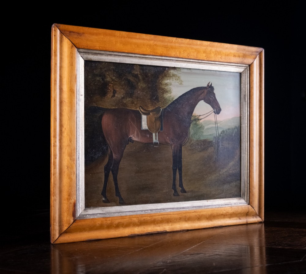 Early 19th-century oil painting on board depicting a saddled bay hunter horse standing in profile within a rural landscape, presented in a light wood frame. View VII