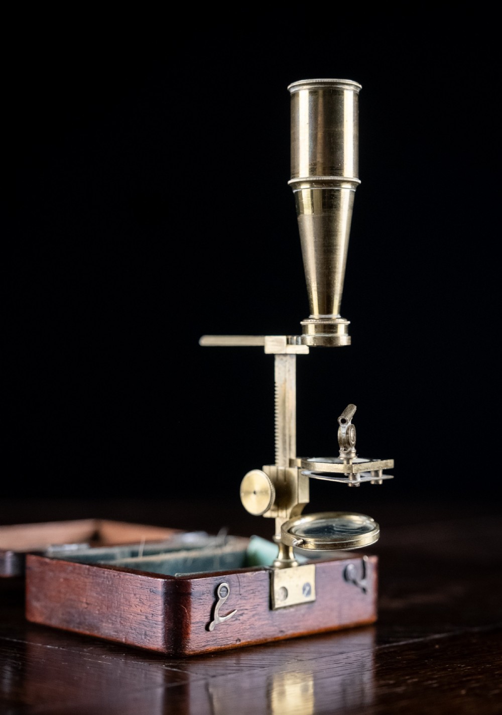 A small early 19th-century lacquered brass pocket microscope mounted onto the rim of its fitted mahogany storage box. View II