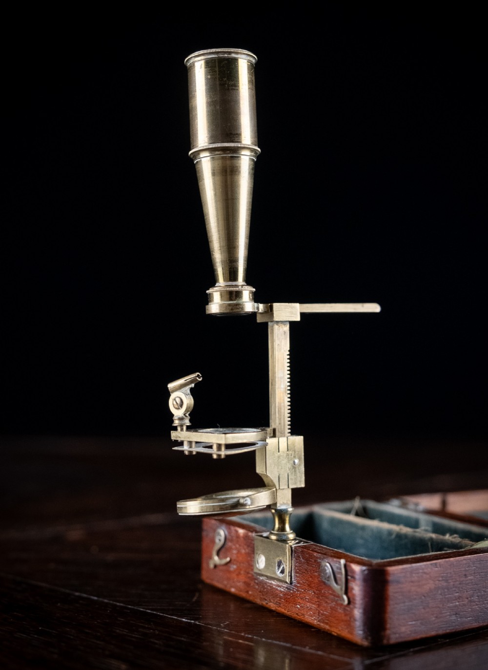 A small early 19th-century lacquered brass pocket microscope mounted onto the rim of its fitted mahogany storage box. View III
