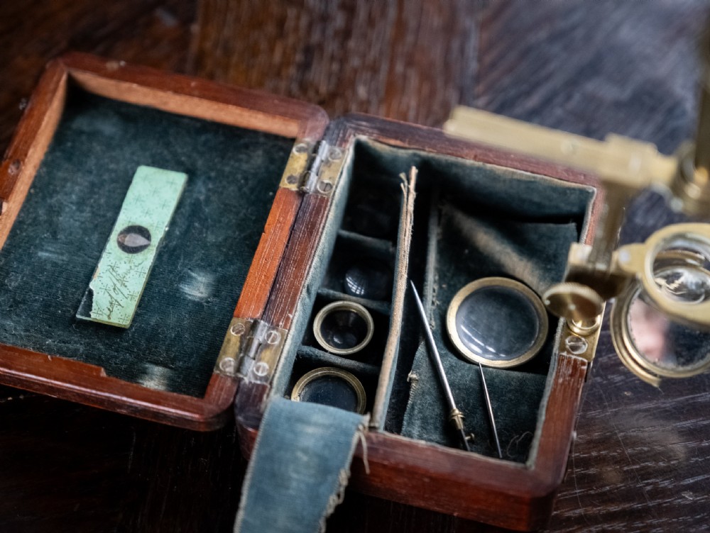 A small early 19th-century lacquered brass pocket microscope mounted onto the rim of its fitted mahogany storage box. View IV