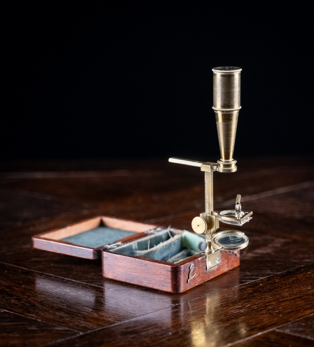 A small early 19th-century lacquered brass pocket microscope mounted onto the rim of its fitted mahogany storage box. View VI