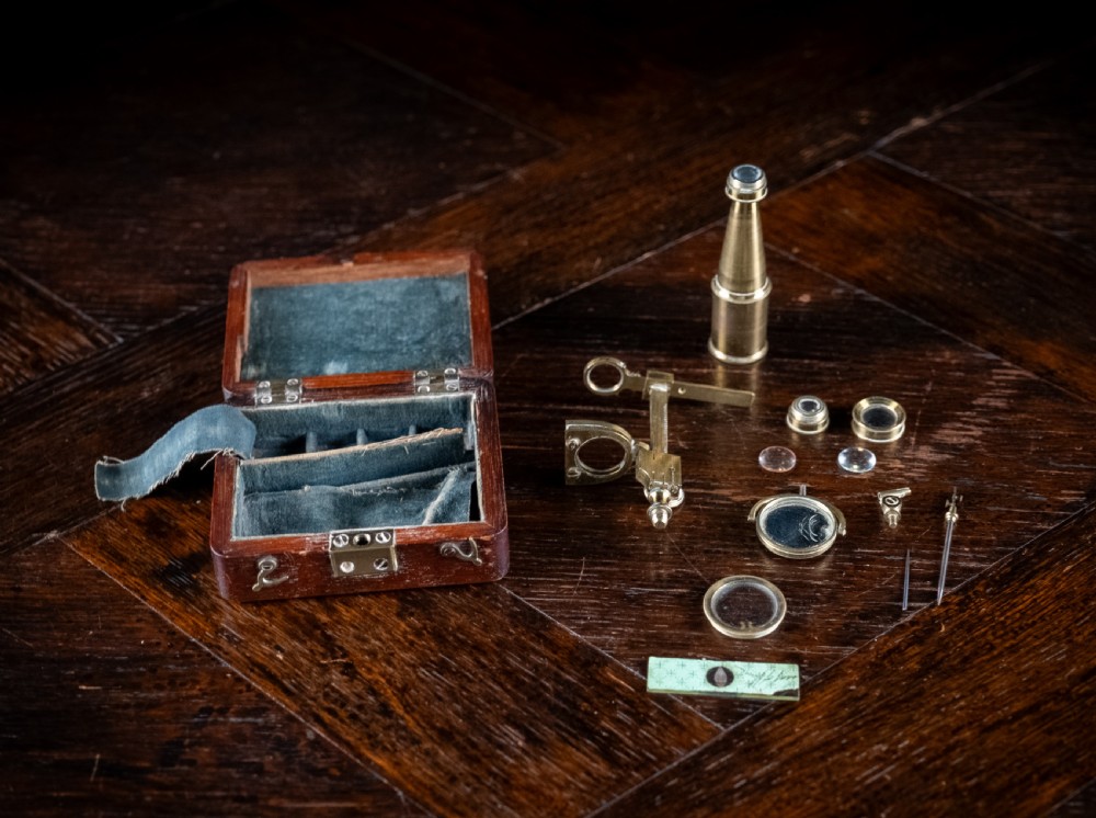 A small early 19th-century lacquered brass pocket microscope mounted onto the rim of its fitted mahogany storage box. View VII