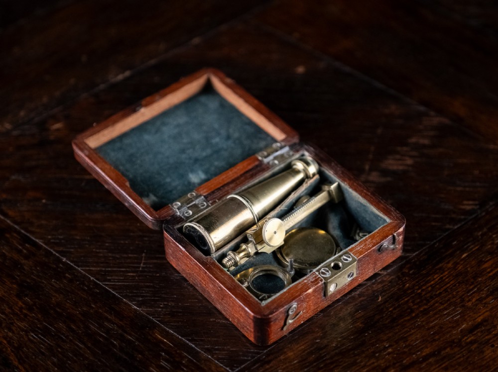 A small early 19th-century lacquered brass pocket microscope mounted onto the rim of its fitted mahogany storage box. View IX