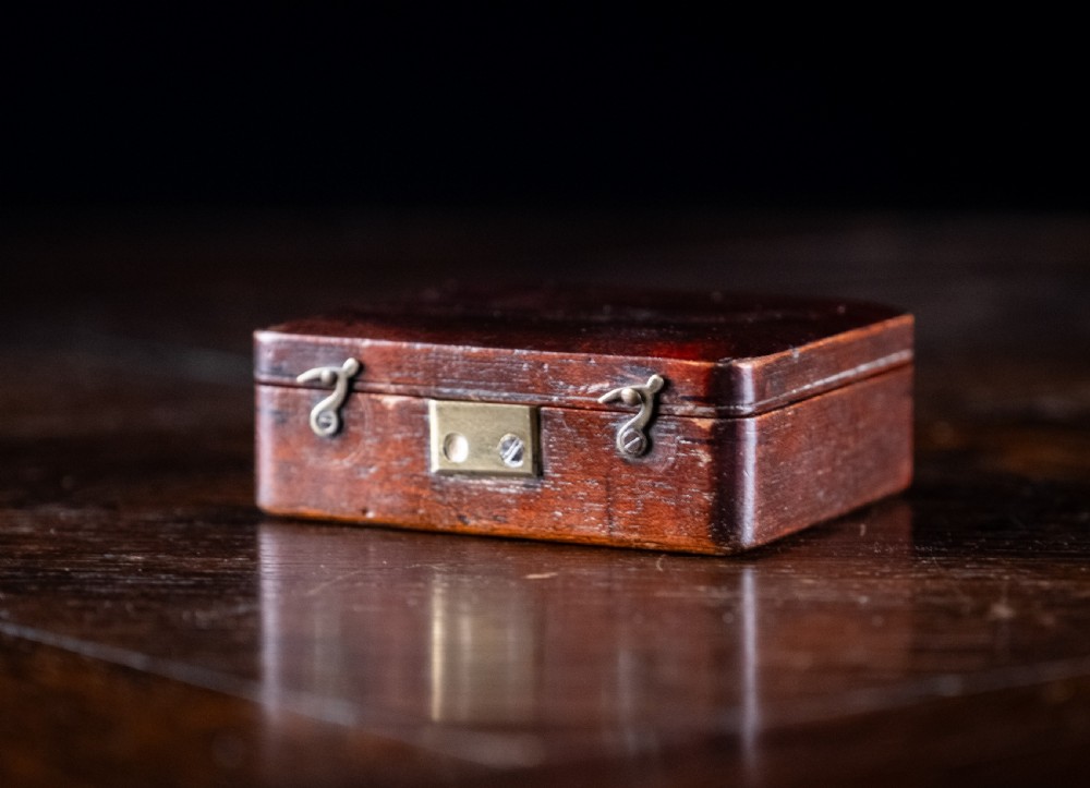 A small early 19th-century lacquered brass pocket microscope mounted onto the rim of its fitted mahogany storage box. View XI