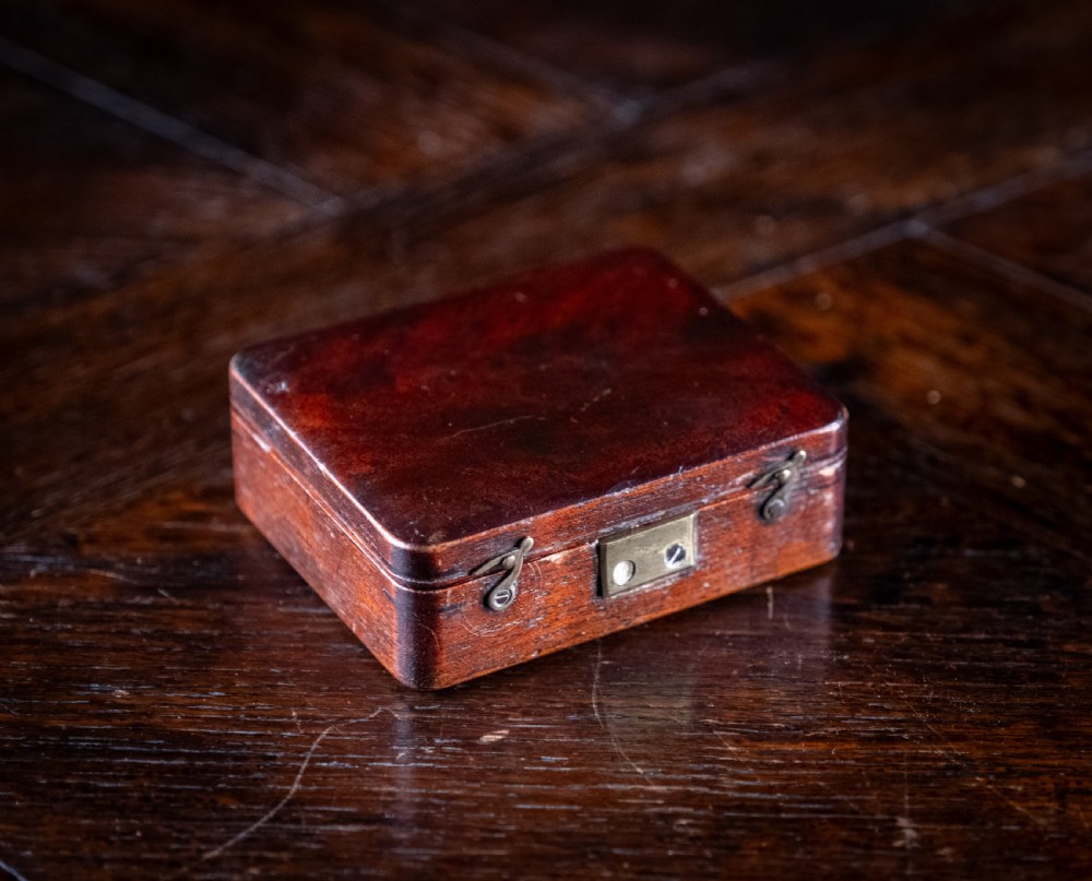 A small early 19th-century lacquered brass pocket microscope mounted onto the rim of its fitted mahogany storage box. View XII