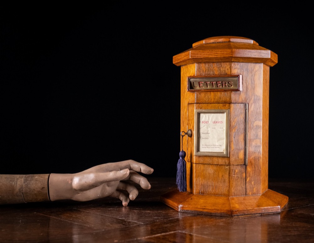 An octagonal oak tabletop post box featuring a brass letter slot marked LETTERS and a key-locked front door with a collection schedule frame. View II