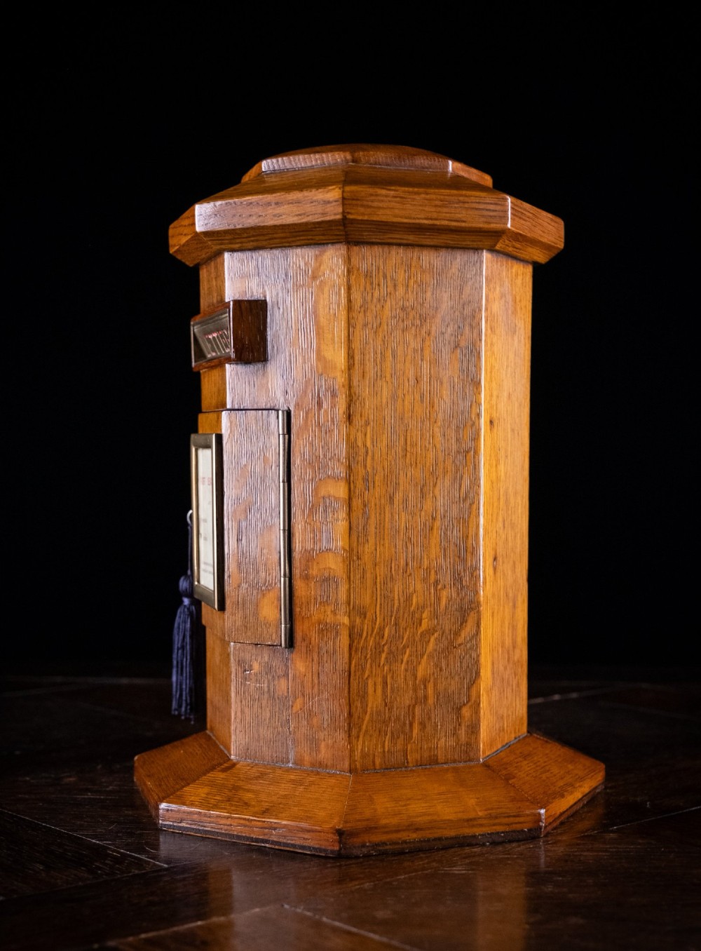 An octagonal oak tabletop post box featuring a brass letter slot marked LETTERS and a key-locked front door with a collection schedule frame. View VI