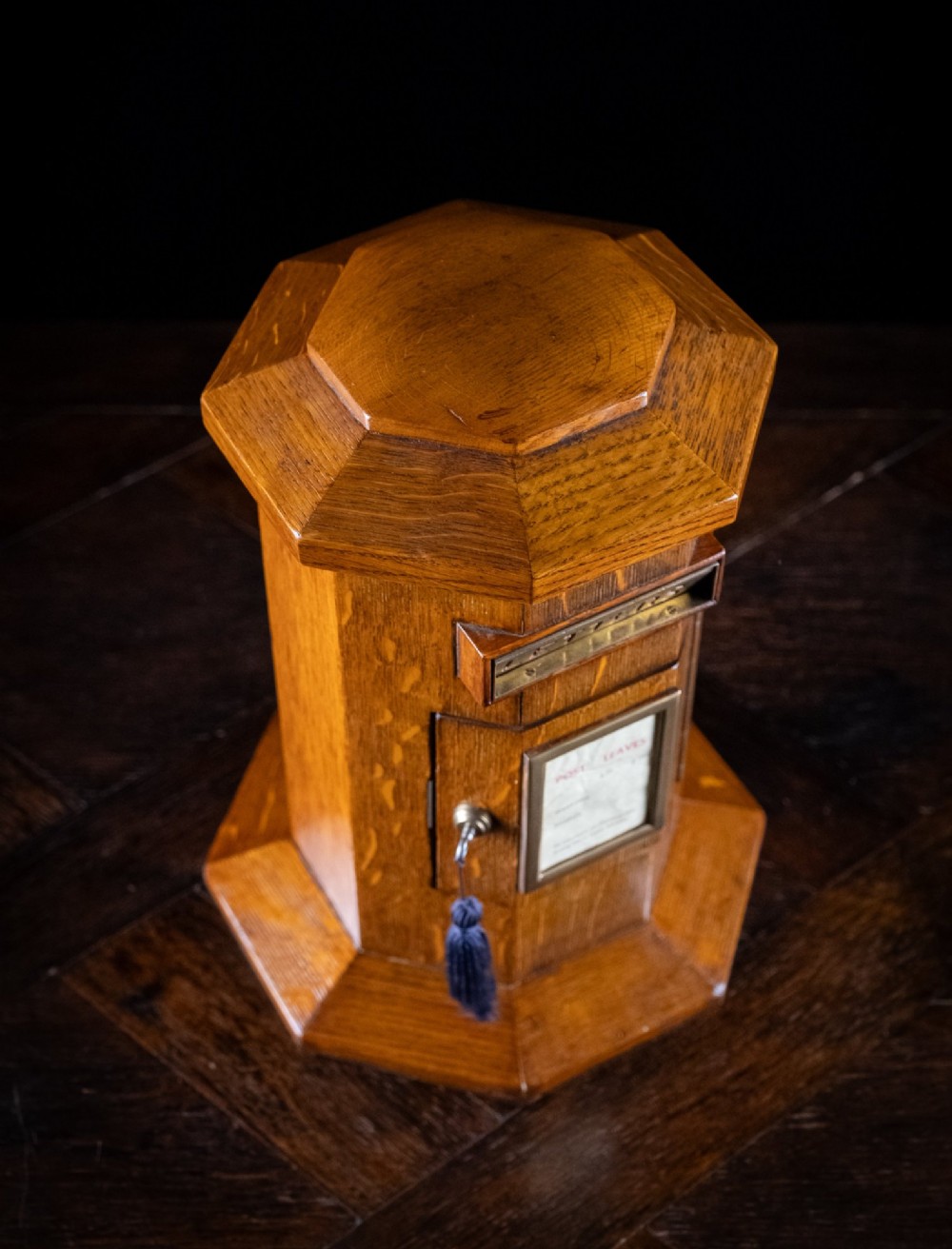 An octagonal oak tabletop post box featuring a brass letter slot marked LETTERS and a key-locked front door with a collection schedule frame. View XI