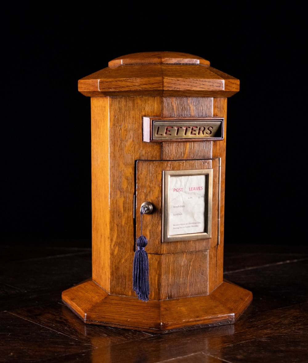 An octagonal oak tabletop post box featuring a brass letter slot marked LETTERS and a key-locked front door with a collection schedule frame. View XII