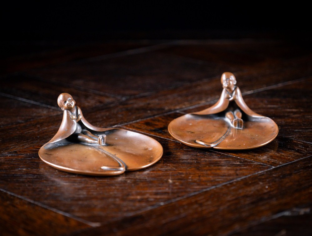 A pair of small, patinated bronze leaf-shaped dishes, each featuring a sculpted figure of a child seated at the folded edge. View II