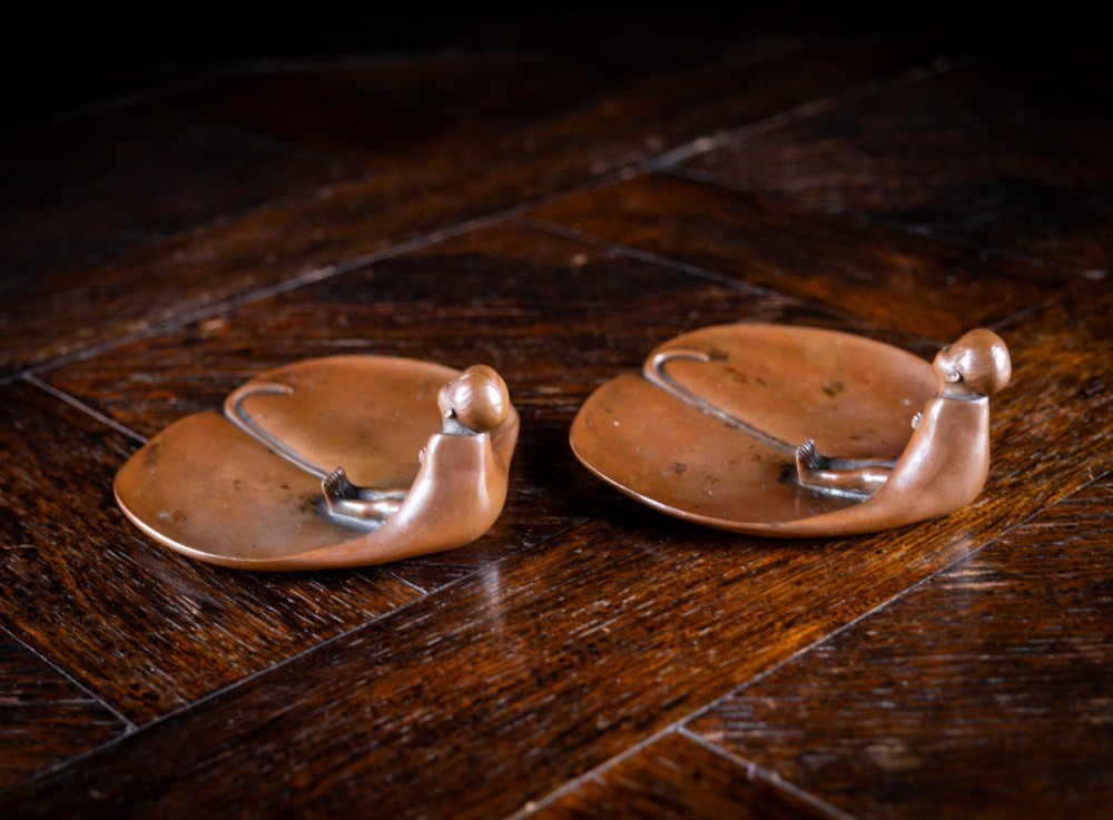 A pair of small, patinated bronze leaf-shaped dishes, each featuring a sculpted figure of a child seated at the folded edge. View V