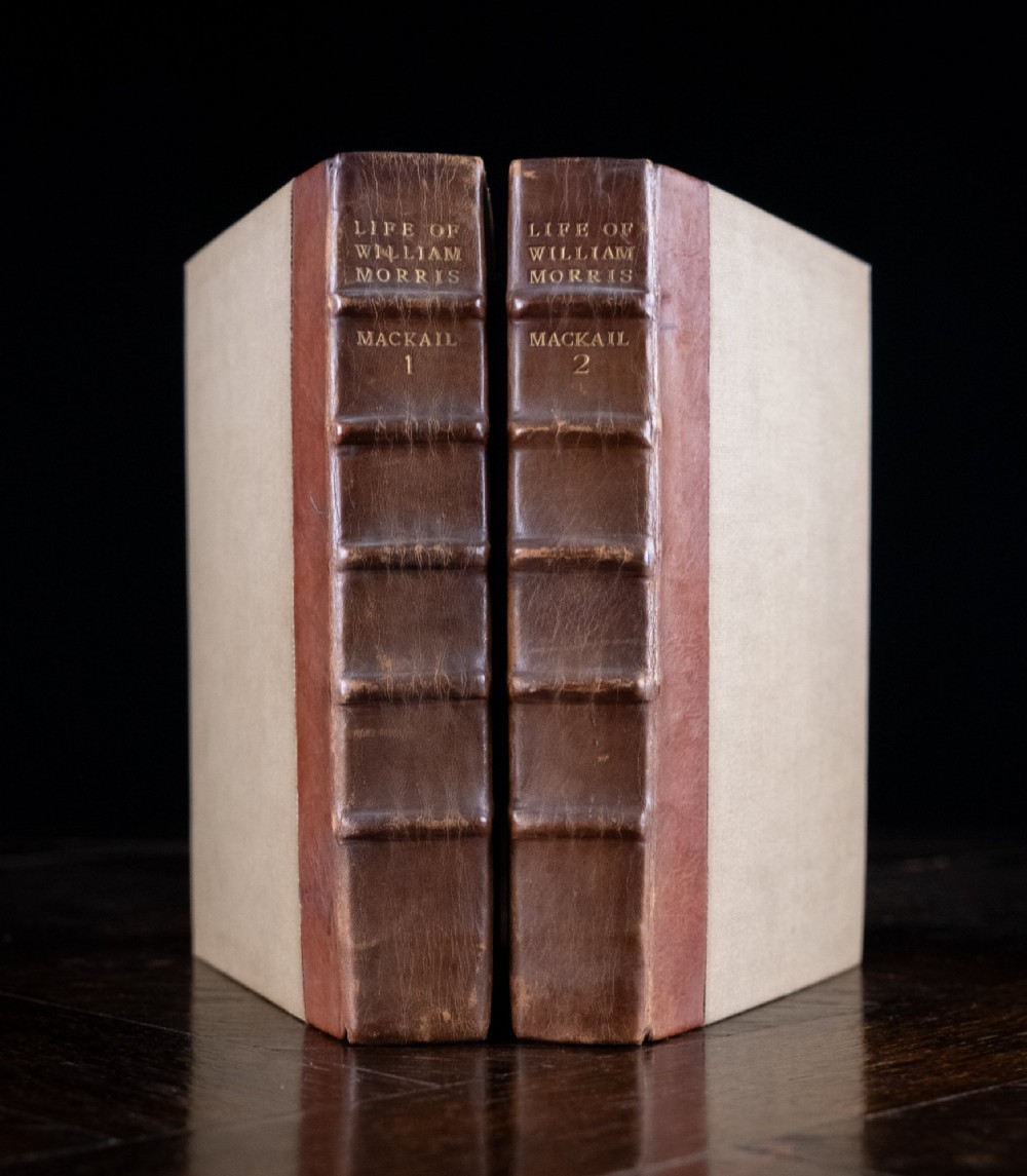 A two-volume set of 1899 first edition books titled The Life of William Morris, bound in brown leather spines with gilt lettering and cream cloth boards.