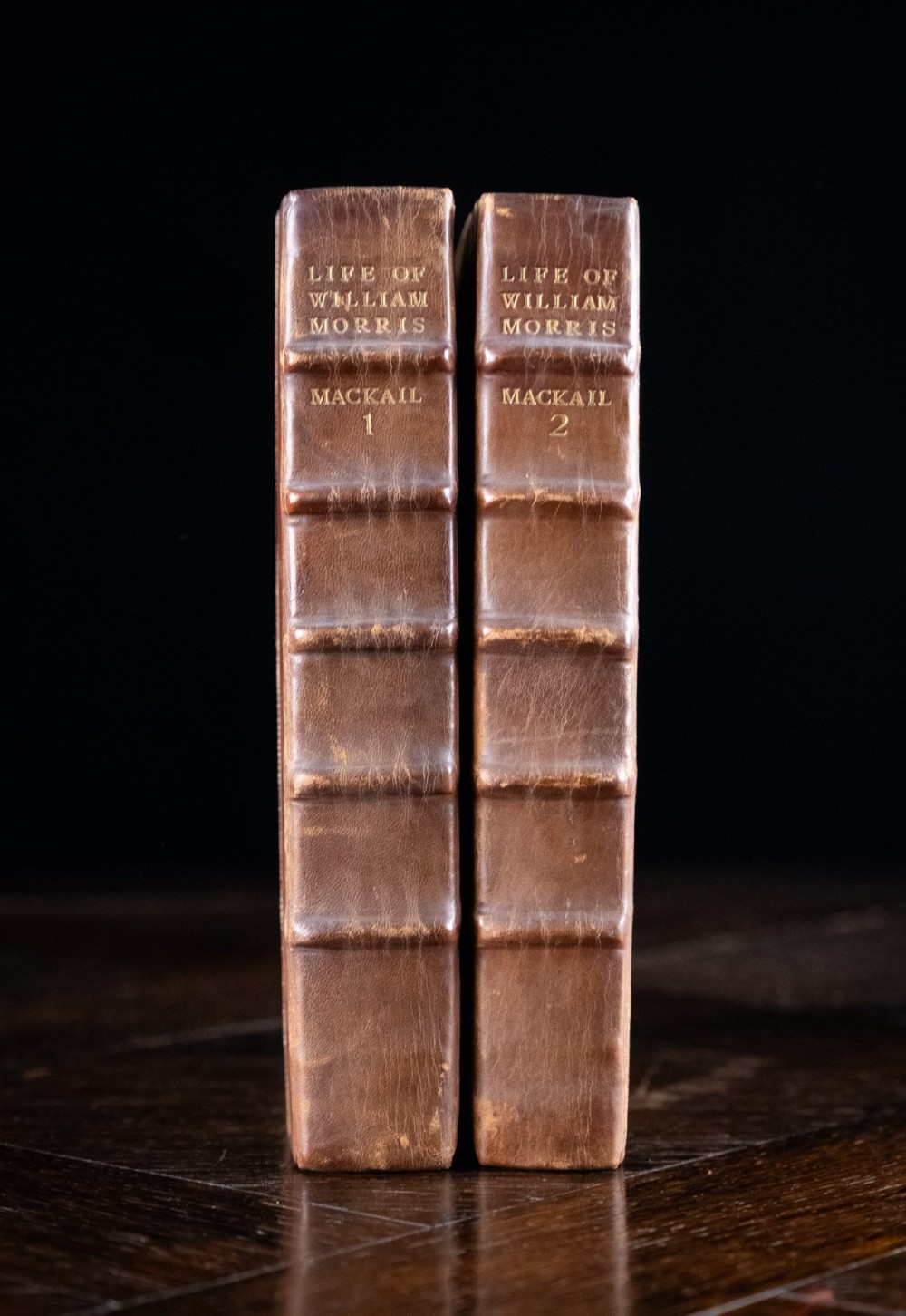 A two-volume set of 1899 first edition books titled The Life of William Morris, bound in brown leather spines with gilt lettering and cream cloth boards. View II
