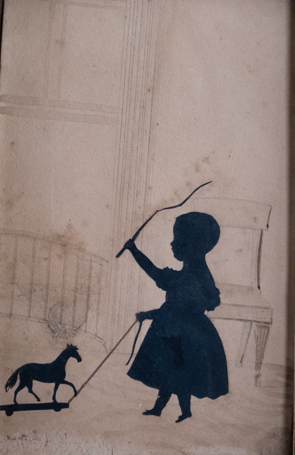A 19th-century cut-paper silhouette depicting a young child pulling a toy horse on wheels, set within a bevelled wooden frame with a gilded inner slip. View II