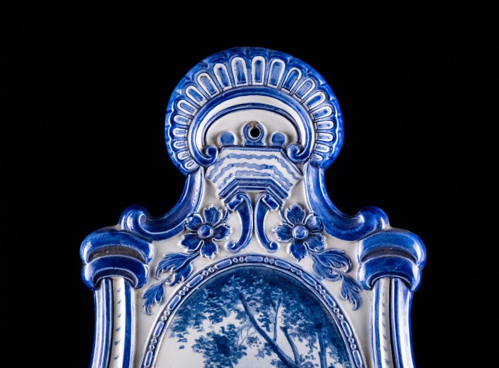 A Rococo Revival blue and white glazed ceramic wall plaque depicting an architectural scene and cherubs, fitted with two gilt ormolu candle branches. View IX