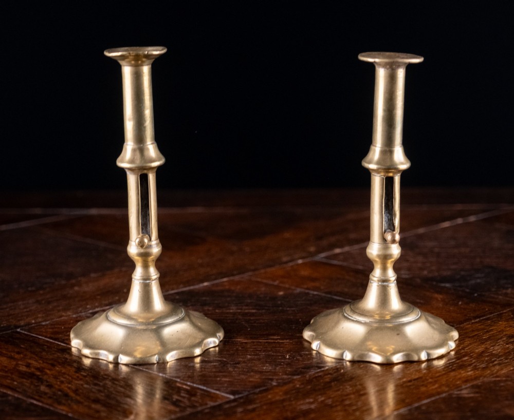A pair of 18th-century cast brass candlesticks featuring turned baluster stems, push-up ejector mechanisms, and scalloped circular bases. View II