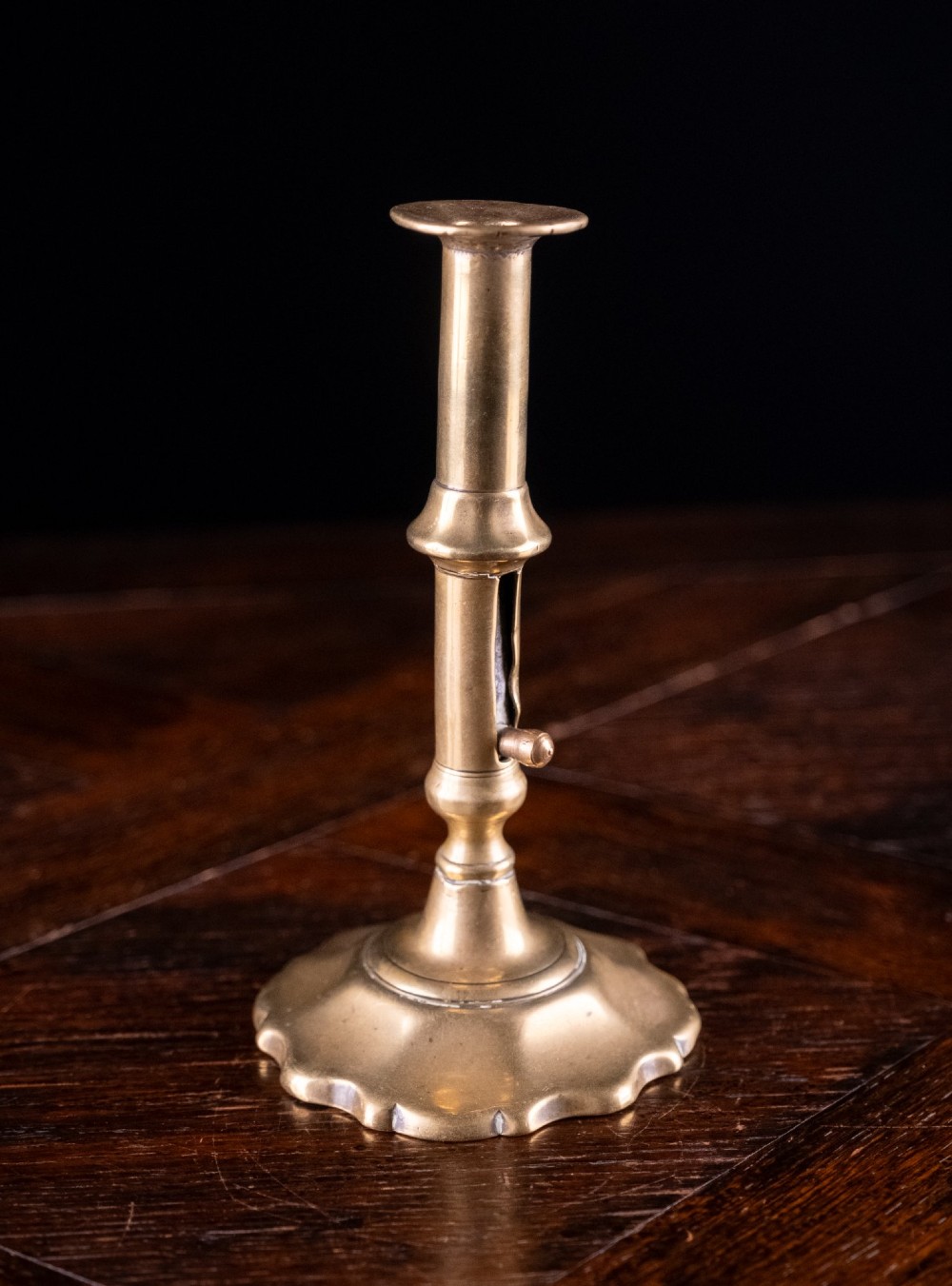 A pair of 18th-century cast brass candlesticks featuring turned baluster stems, push-up ejector mechanisms, and scalloped circular bases. View V