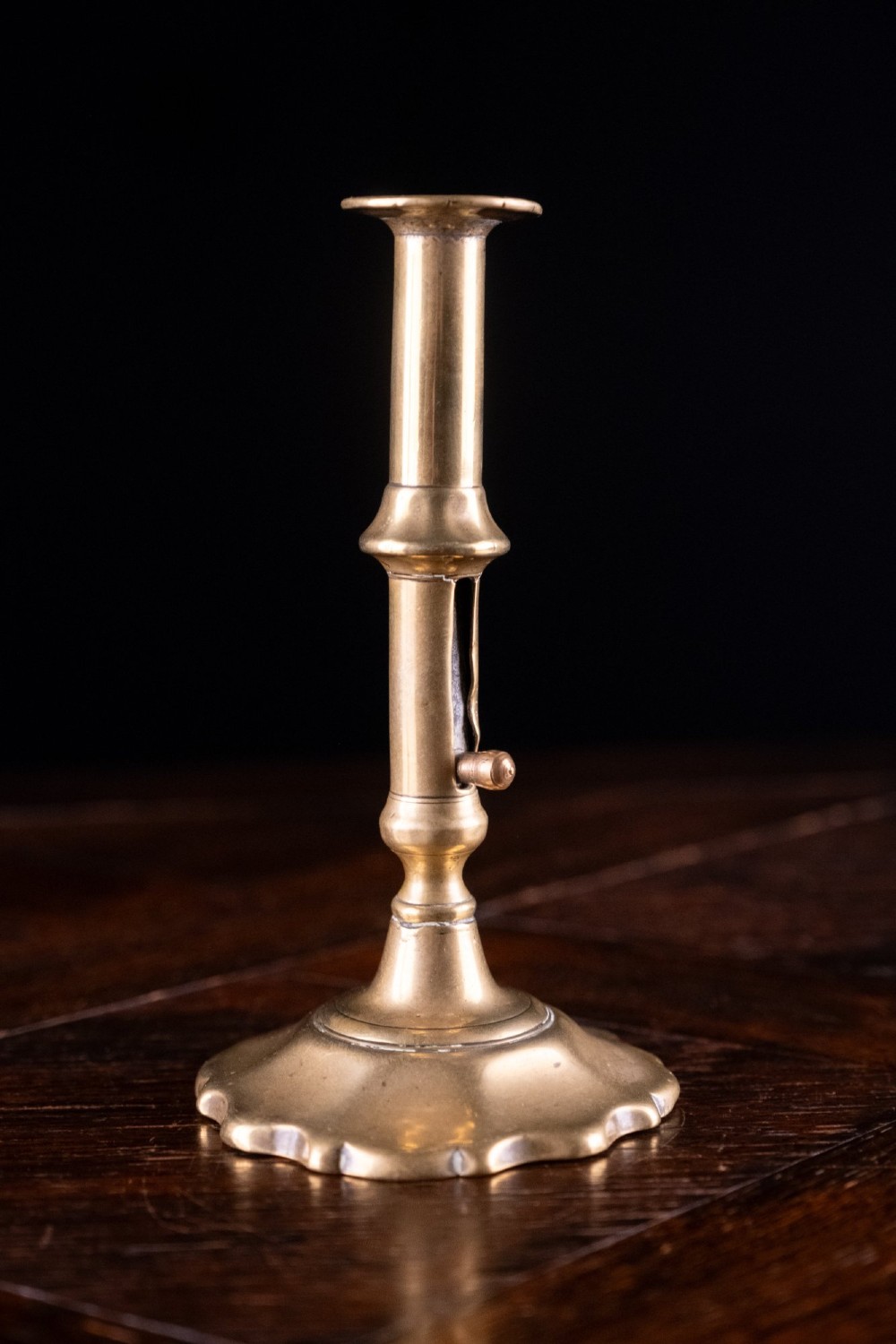 A pair of 18th-century cast brass candlesticks featuring turned baluster stems, push-up ejector mechanisms, and scalloped circular bases. View VI