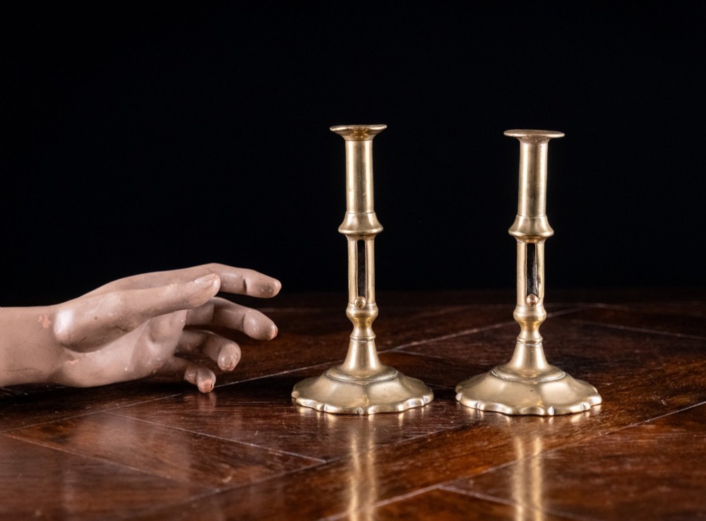 A pair of 18th-century cast brass candlesticks featuring turned baluster stems, push-up ejector mechanisms, and scalloped circular bases. View VIII