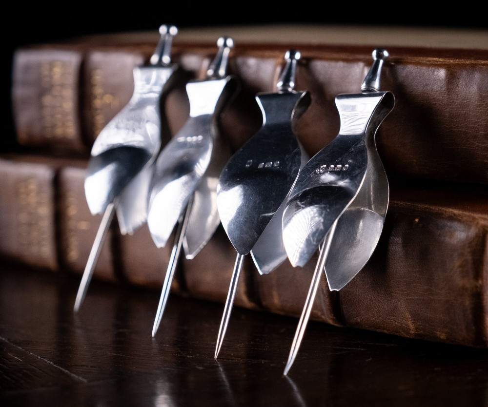 A set of four solid sterling silver lemon wedge squeezers featuring hinged mechanical presses and English hallmarks.