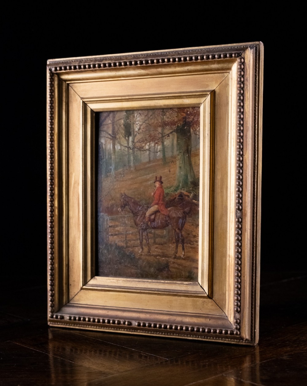 A 19th-century oil painting on panel depicting a gentleman in a red hunting coat atop a horse next to a timber gate in autumn woods. View VIII
