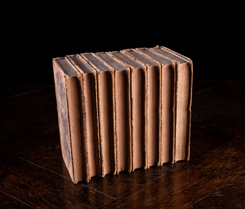 An eight-volume set of 18th-century leather-bound books standing upright with visible raised spine bands and gilt titles. View V