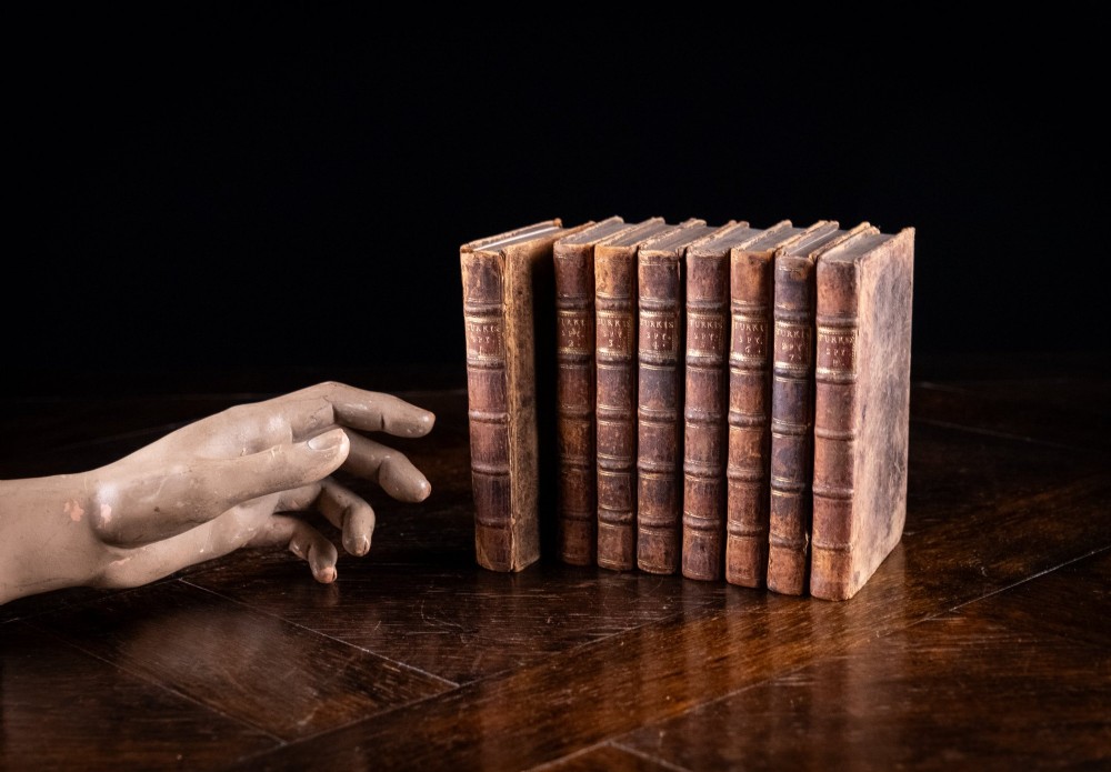 An eight-volume set of 18th-century leather-bound books standing upright with visible raised spine bands and gilt titles. View XI