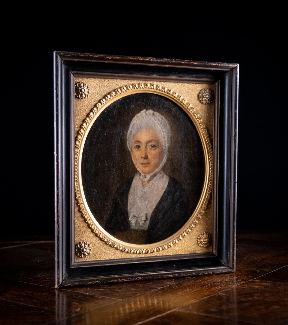 An 18th-century oil painting depicting a lady in a white lace cap and dark garment, framed within a gilded oval slip set inside a rectangular dark wooden frame. View V
