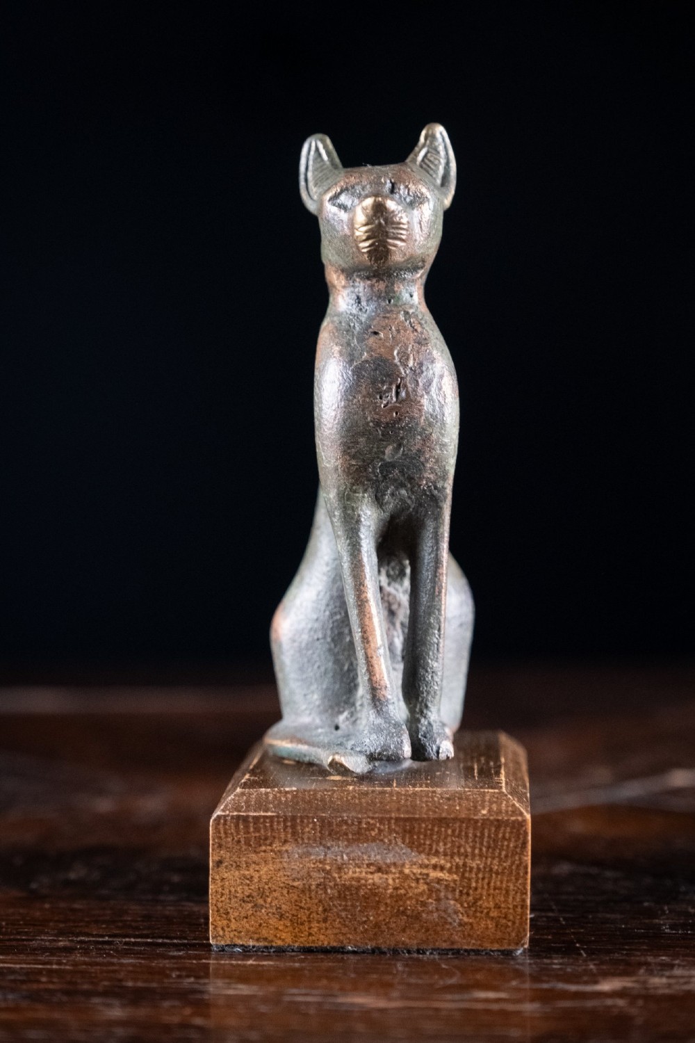 A patinated bronze sculpture of an upright seated Egyptian cat mounted on a rectangular wooden plinth base. View III