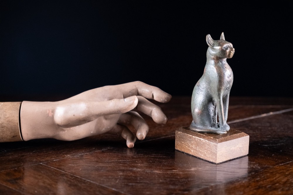 A patinated bronze sculpture of an upright seated Egyptian cat mounted on a rectangular wooden plinth base. View VII
