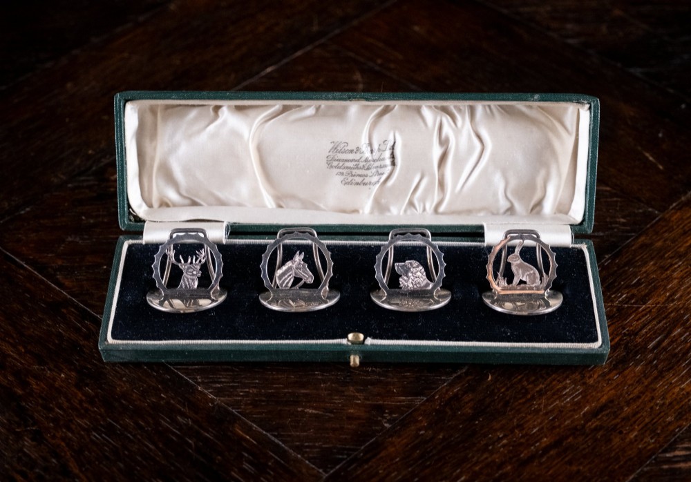 A set of four sterling silver animal-themed menu holders featuring a stag, horse, dog, and hare, presented inside a fitted green display box. View VI