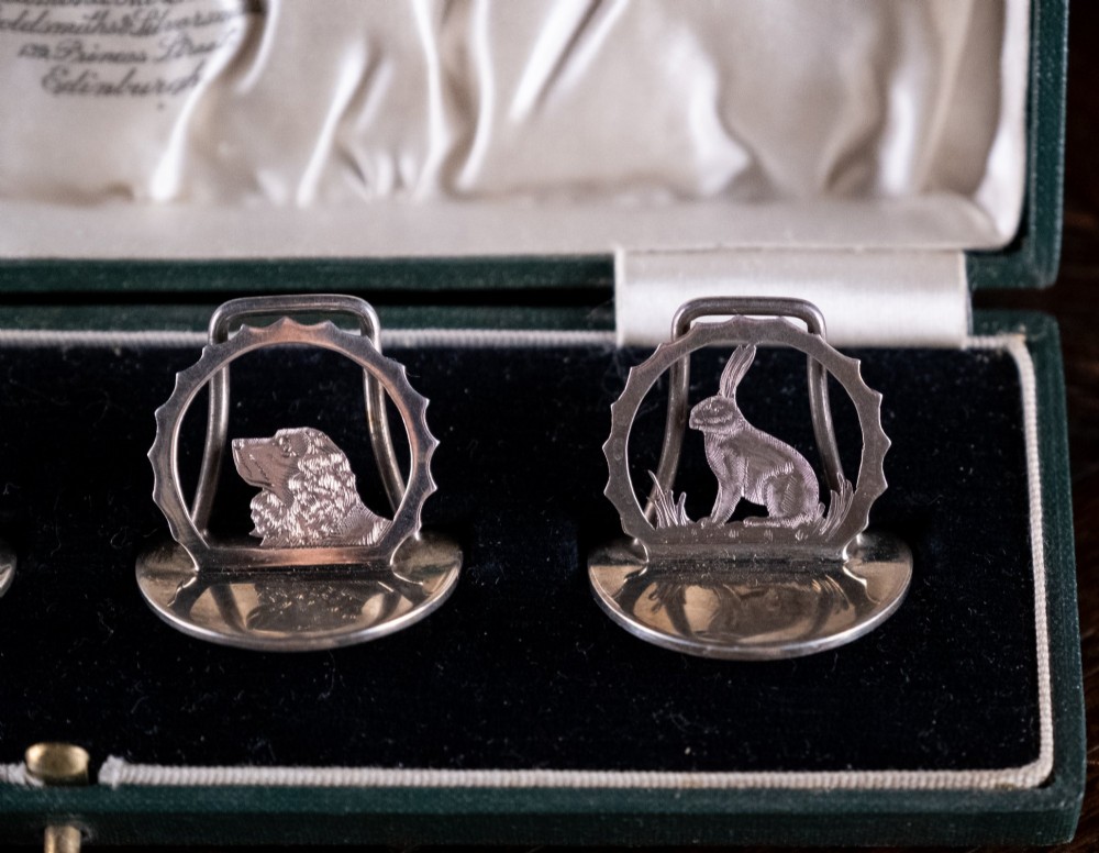 A set of four sterling silver animal-themed menu holders featuring a stag, horse, dog, and hare, presented inside a fitted green display box. View VIII